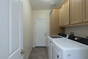 A laundry room with a white door, wooden cabinets, and a front-loading washer and dryer. - 360 degree vineyard views on 2 acres, patio, outdoor kitchen, game-room, dogs ok (Paso Robles)