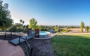 A backyard with a hot tub, a wooden deck, and a view of vineyards.
