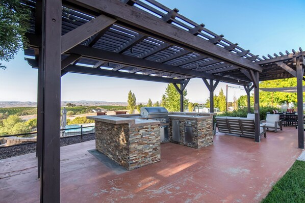 An outdoor patio with a stone barbecue and grill area, surrounded by a pergola.
