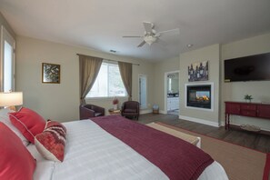 A hotel room with a bed, a fireplace, a television, and a ceiling fan.