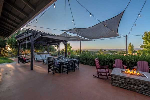 An outdoor patio with a pergola, dining table, chairs, and a fire feature.