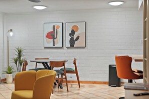 Ein modernes Interieur mit einer Ziegelwand, zwei gerahmten Kunstwerken, einem runden Tisch mit Stühlen und einem Topfpflanzen.