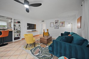 Uma sala de estar com sofá, uma poltrona amarela, televisão e ventilador de teto.