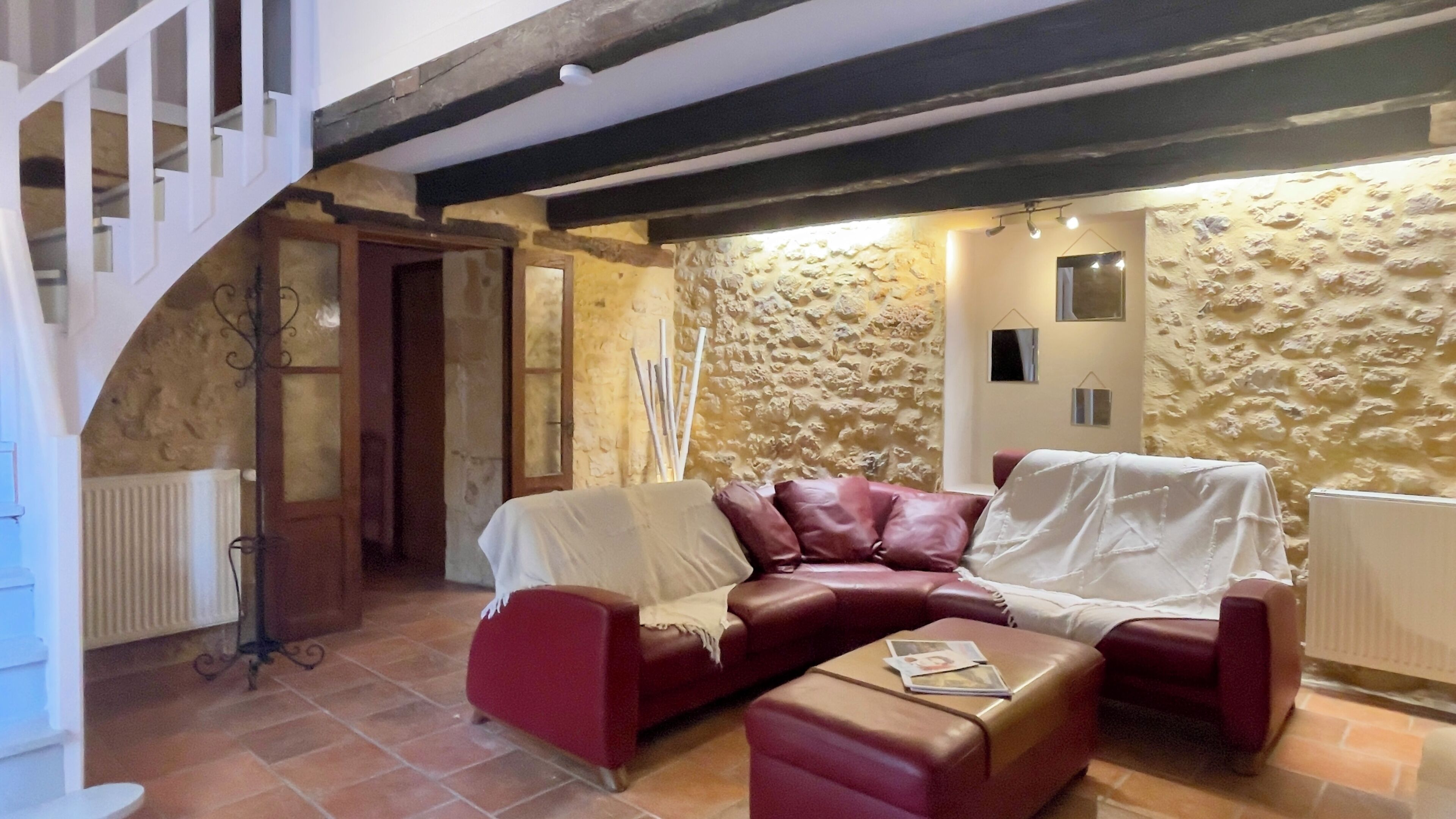 Ein gemütliches Wohnzimmer mit einer Steinwand, einem roten Ledersofa, einem abgedeckten Couchtisch und einer Treppe.