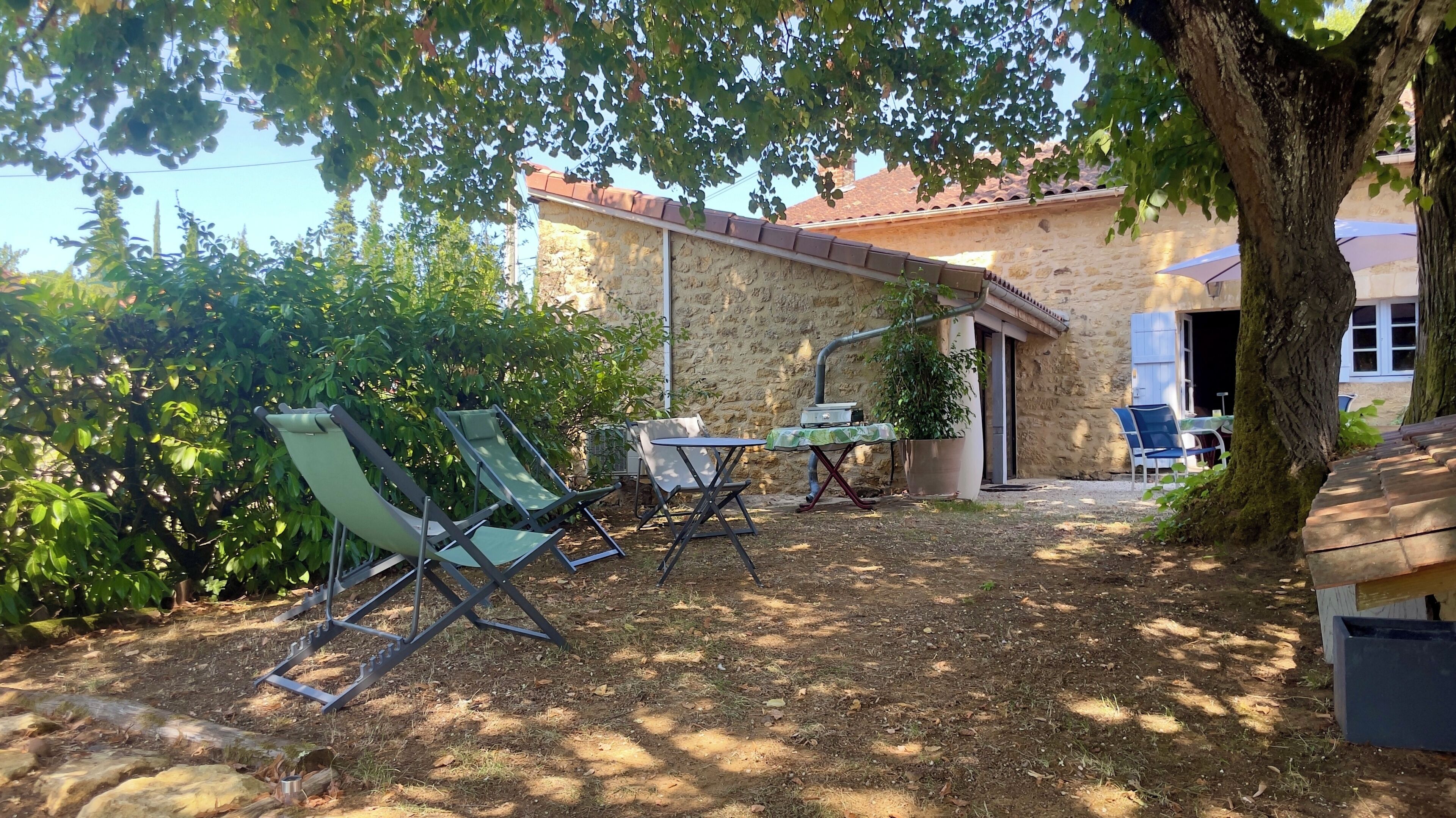 Un espace patio aménagé avec du mobilier d’extérieur, un mur en pierre et un arbre qui offre de l’ombre.