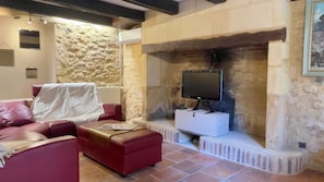 A living room with a stone wall, a red sofa, a white ottoman, and a flat-screen TV mounted on the wall.