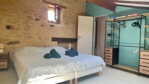 A bedroom with a stone wall, a bed with a patterned bedspread, a wardrobe with a mirror, and a small window.