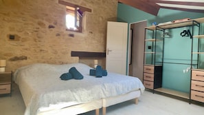 A bedroom with a stone wall, a bed with a patterned bedspread, a wardrobe with a mirror, and a small window.