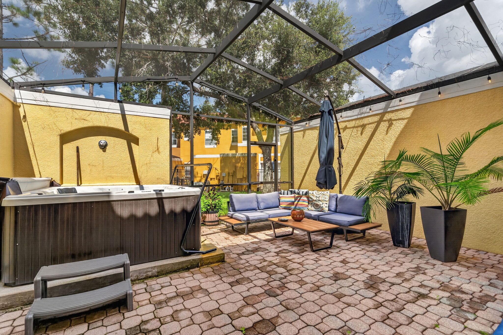 An outdoor patio with a covered seating area, a barbecue grill, and potted plants.
