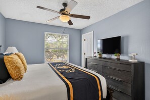 Quarto com cama, penteadeira, ventilador de teto, janela com persianas e televisão.
