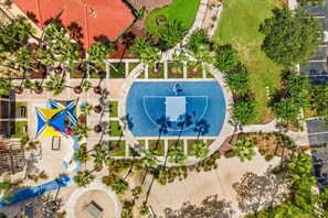 Vue aérienne d’un parc comprenant un terrain de basketball, une aire de jeux et de la végétation environnante.