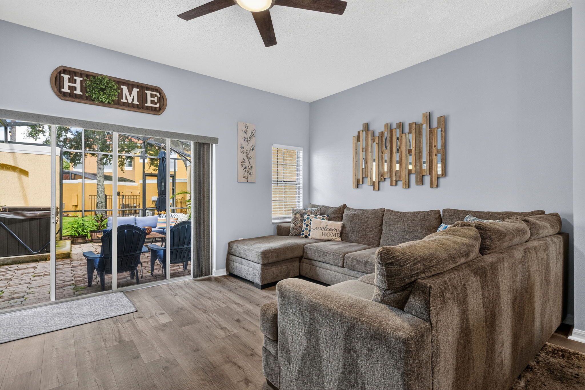 A living room with a sectional sofa, a ceiling fan, and a sliding glass door leading to an outdoor patio.