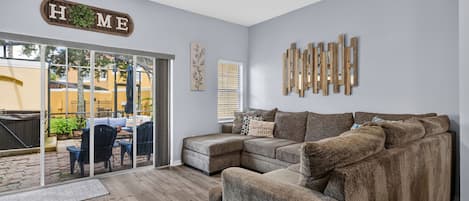 A living room with a sectional sofa, a ceiling fan, and a sliding glass door leading to an outdoor patio.