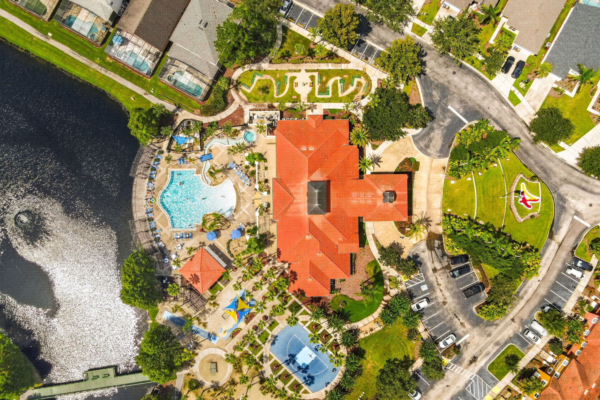 An aerial view of a resort with multiple swimming pools, a large central building, and a parking area.