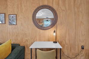A room with a wooden paneled wall, a round mirror, a white desk, a chair, and a lamp. - Brand new Cozy 1-bedroom building in charming Lake Placid with AC (Lake Placid)