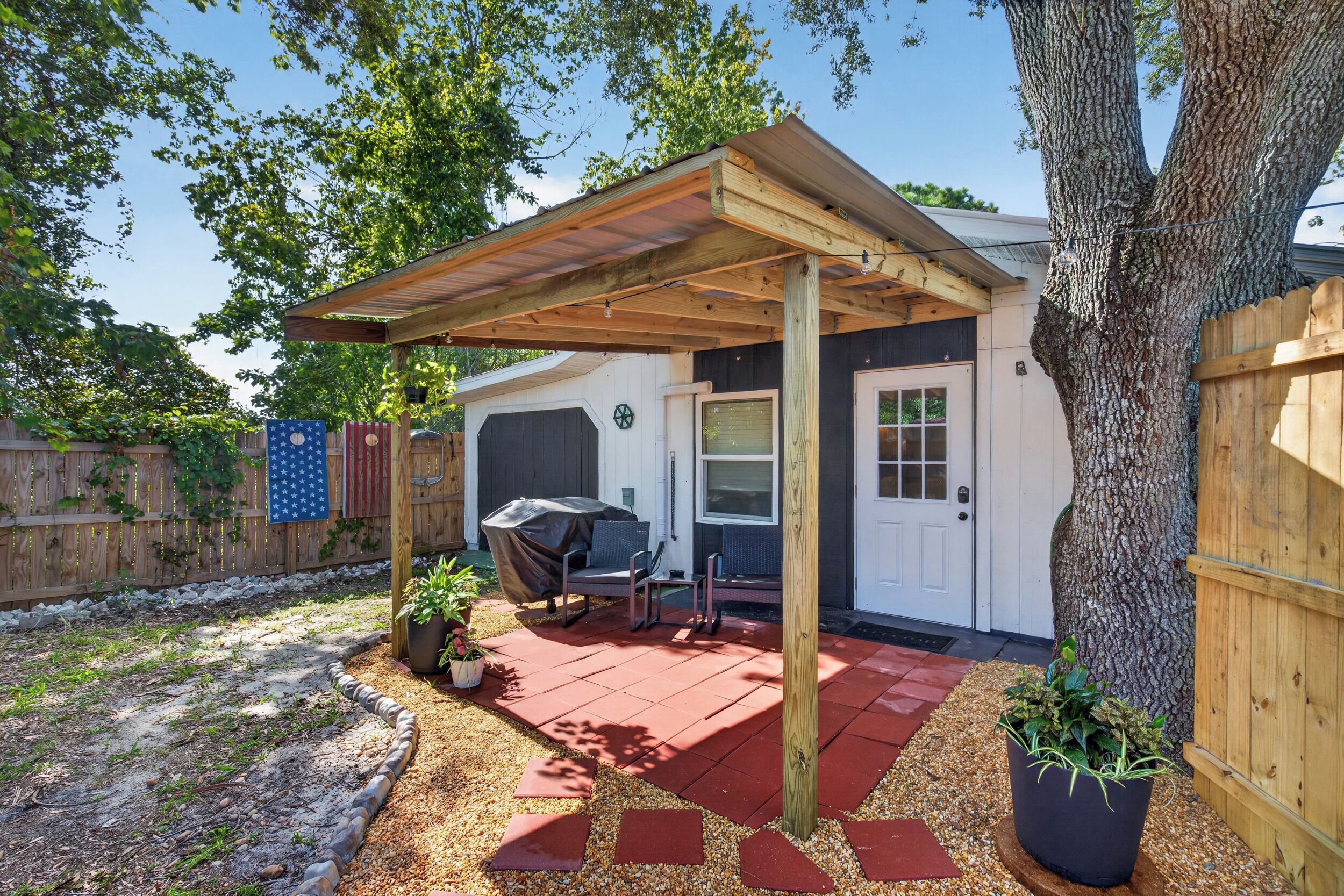Un patio cubierto con una parrilla, asientos exteriores y un árbol.