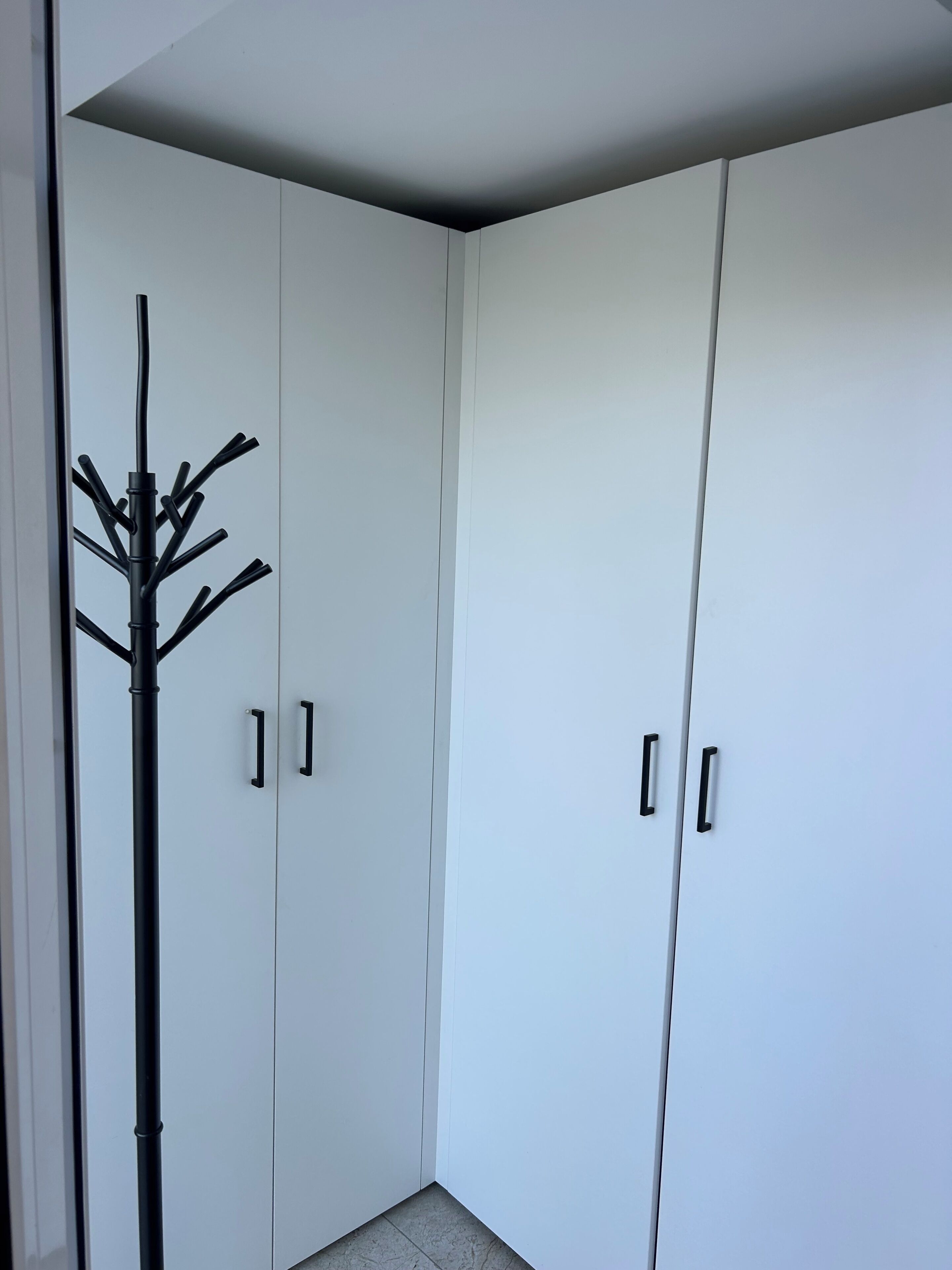A corner of a room with white wardrobes and a black coat stand.