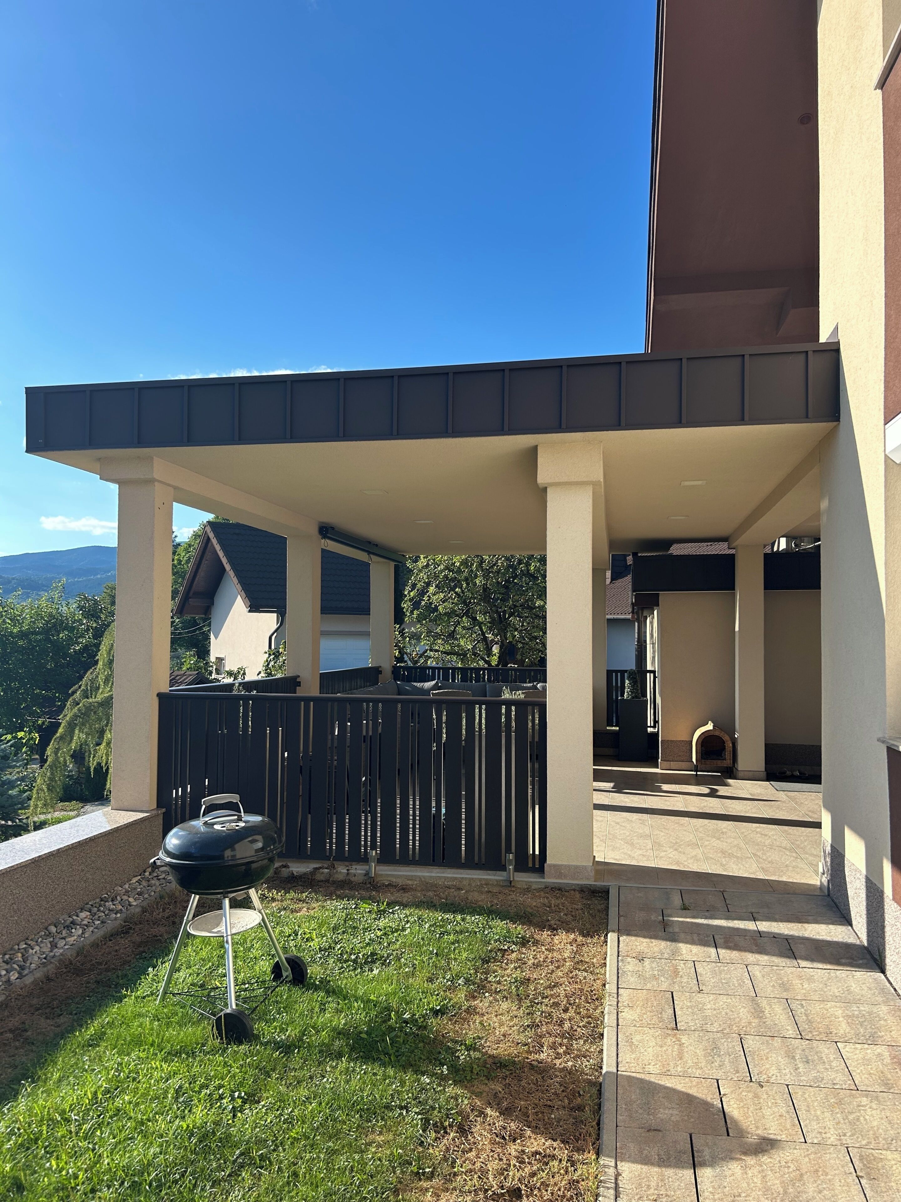 A covered outdoor area with a barbecue grill, a fenced patio, and a view of a mountain range.