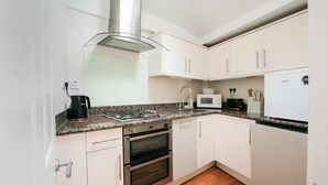 A kitchen with white cabinets, a stainless steel range hood, a gas stove, a microwave, and a toaster. - Entire Westminster Townhouse Near WestminsterAbbey (London)