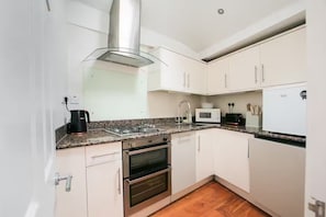 A kitchen with white cabinets, a stainless steel range hood, a gas stove, a microwave, and a toaster. - Entire Westminster Townhouse Near WestminsterAbbey (London)