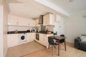 A compact kitchen with a dining area, a washing machine, a microwave, and a stove. - Entire Westminster Townhouse Near WestminsterAbbey (London)