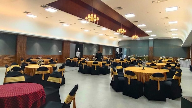 A banquet hall with round tables and chairs, a stage, and a chandelier.