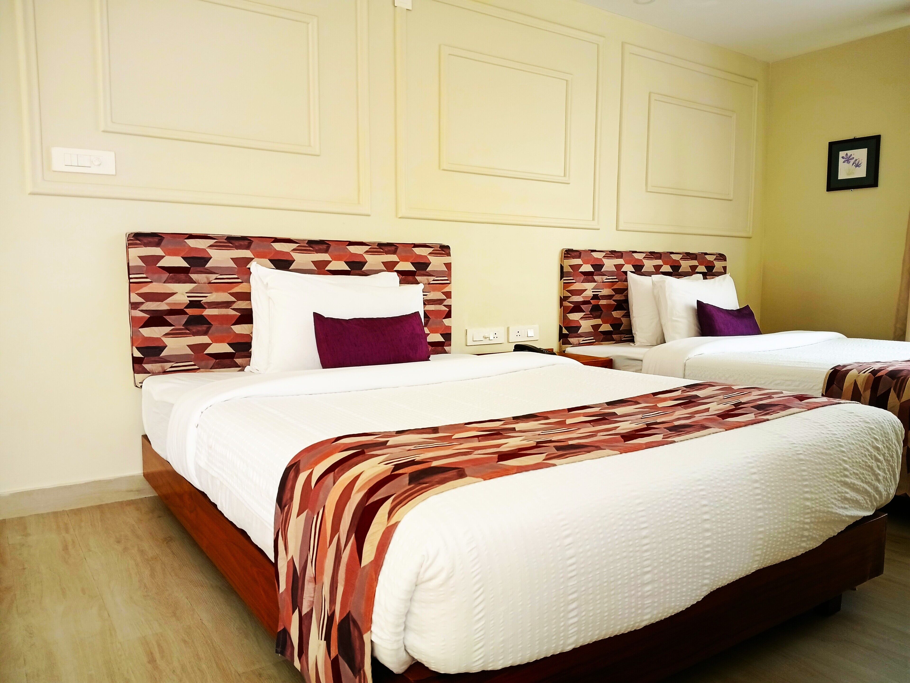 Een hotelkamer met twee bedden, elk met een gestreept hoofdeinde, witte beddengoed en een paars kussen.