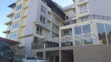 Un edificio residencial de varios pisos con techo plano, balcones y zona de estacionamiento techada.