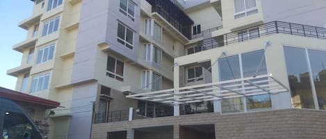 A multi-story residential building with a flat roof, balconies, and a covered parking area.