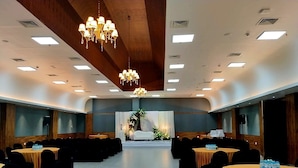 A conference room with round tables, black chairs, a stage with floral decorations, and a chandelier.