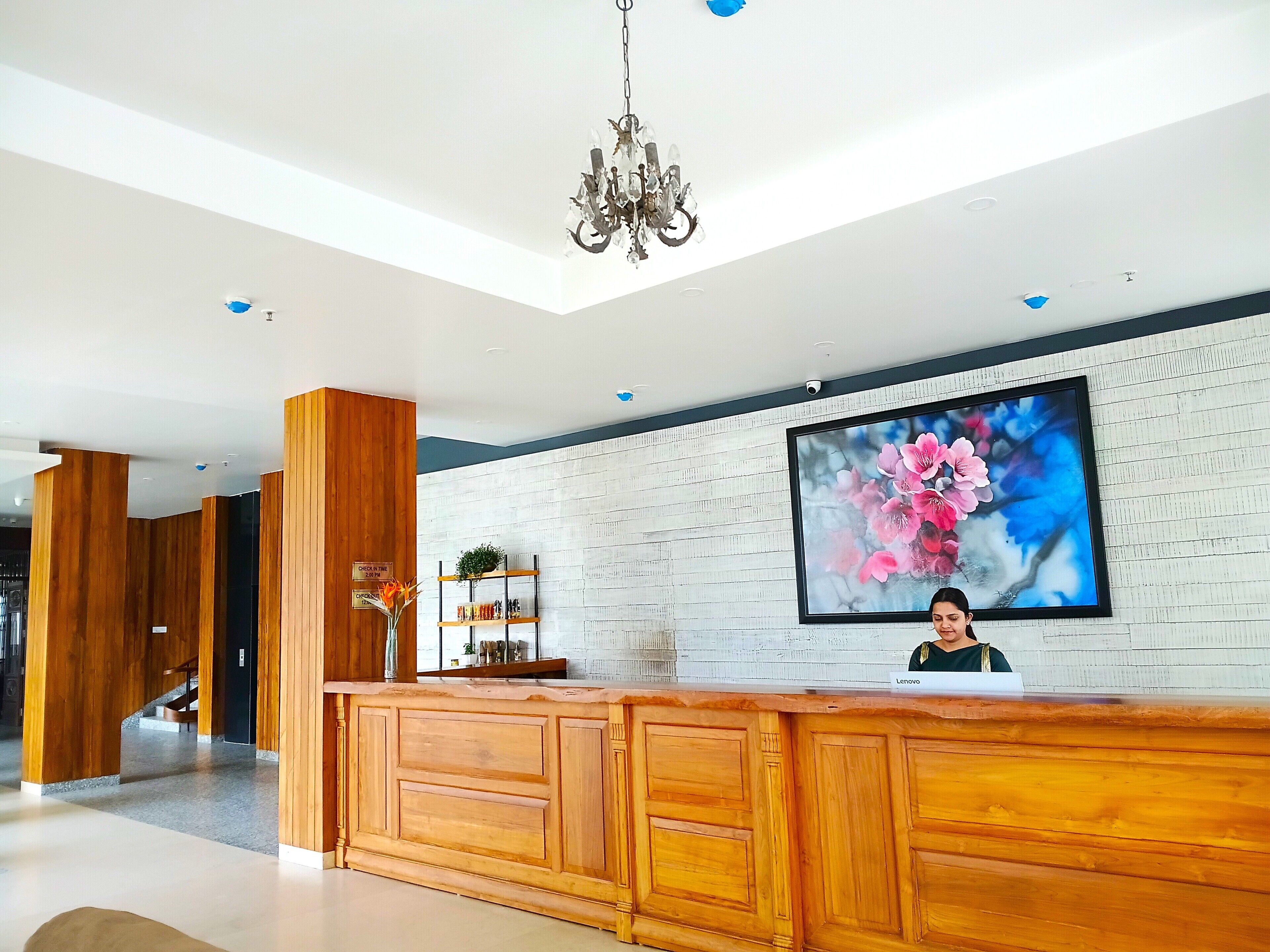A reception desk with a wooden finish, a chandelier, and a large floral artwork on the wall.