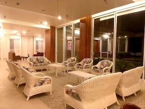 A spacious indoor area with wicker furniture, a glass partition, and a view of the outdoors.