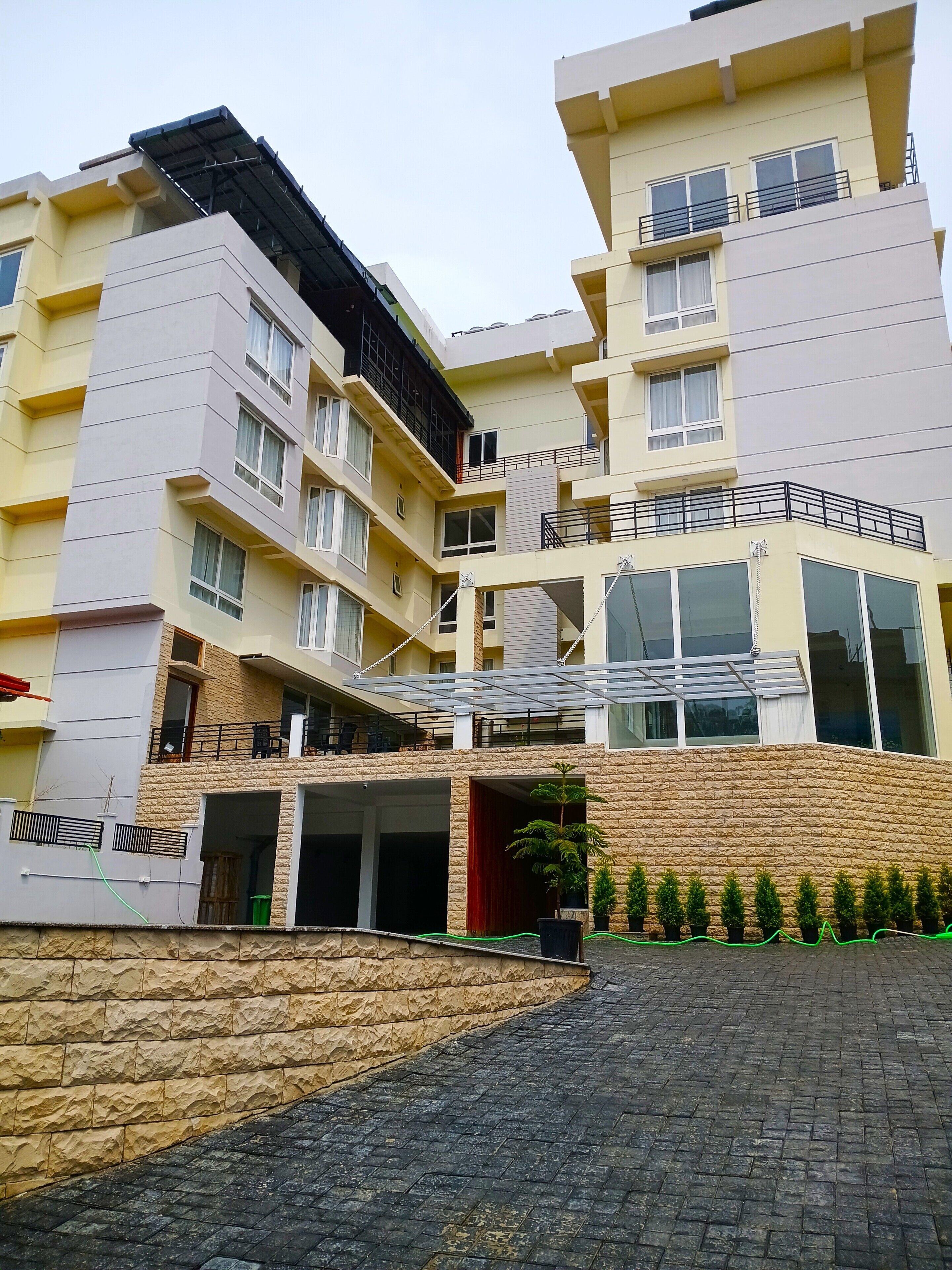 A multi-story hotel with a modern design, featuring balconies, a covered entrance, and a landscaped area with potted plants.