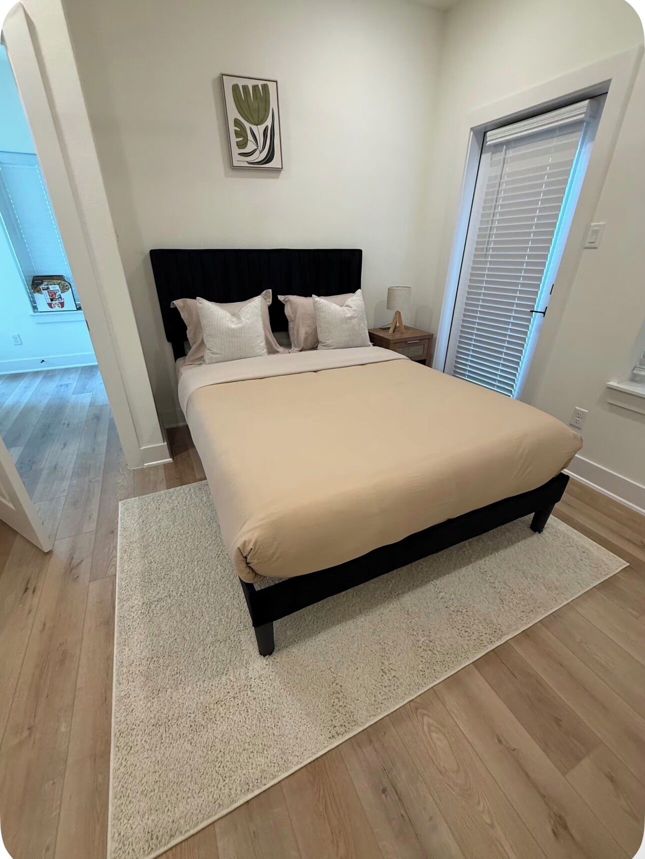 A bedroom with a bed, a nightstand, a lamp, a wall art piece, and a window with blinds.