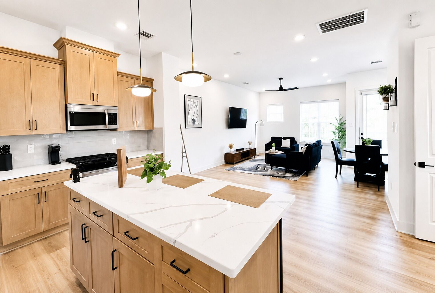 A modern kitchen with wooden cabinets, a central island, and a dining area with a black sofa and table.