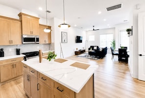 Een moderne keuken met houten kastjes, een centraal eiland en een zithoek met een zwarte bank en tafel.
