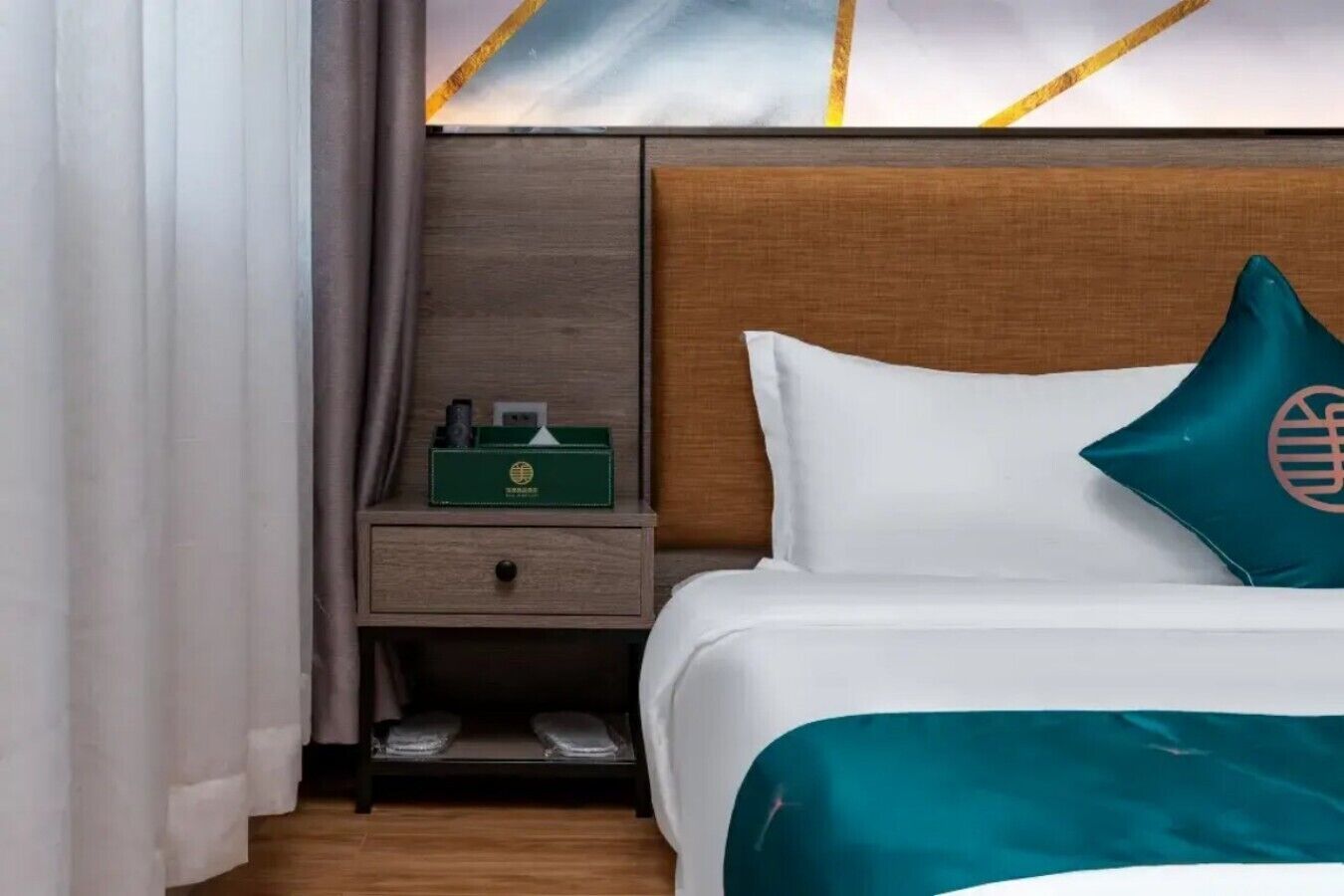 A hotel room with a bed, a nightstand, a green box, and a pillow with a globe design.