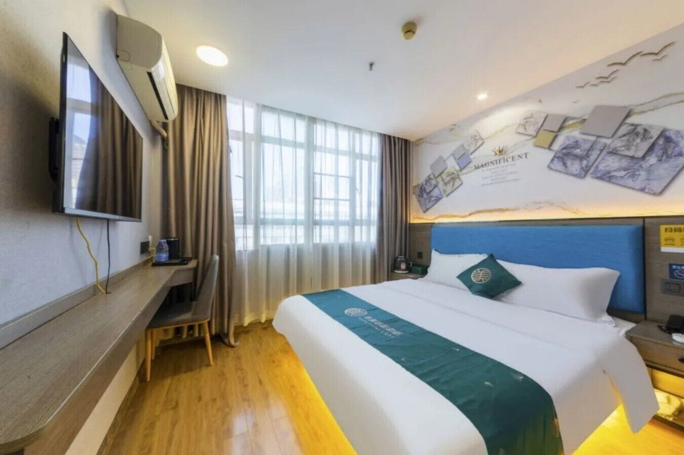 Ein Hotelzimmer mit Bett, Schreibtisch, Fernseher und einem großen Fenster.