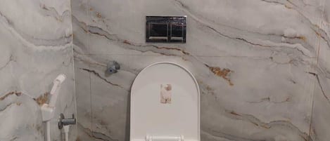 Baño con pared de mármol, inodoro blanco, ducha y cabezal de ducha de mano.