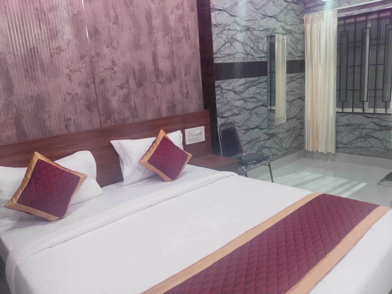 Habitación de hotel con cama, cabecera de madera, pared de mármol y una ventana con cortinas.