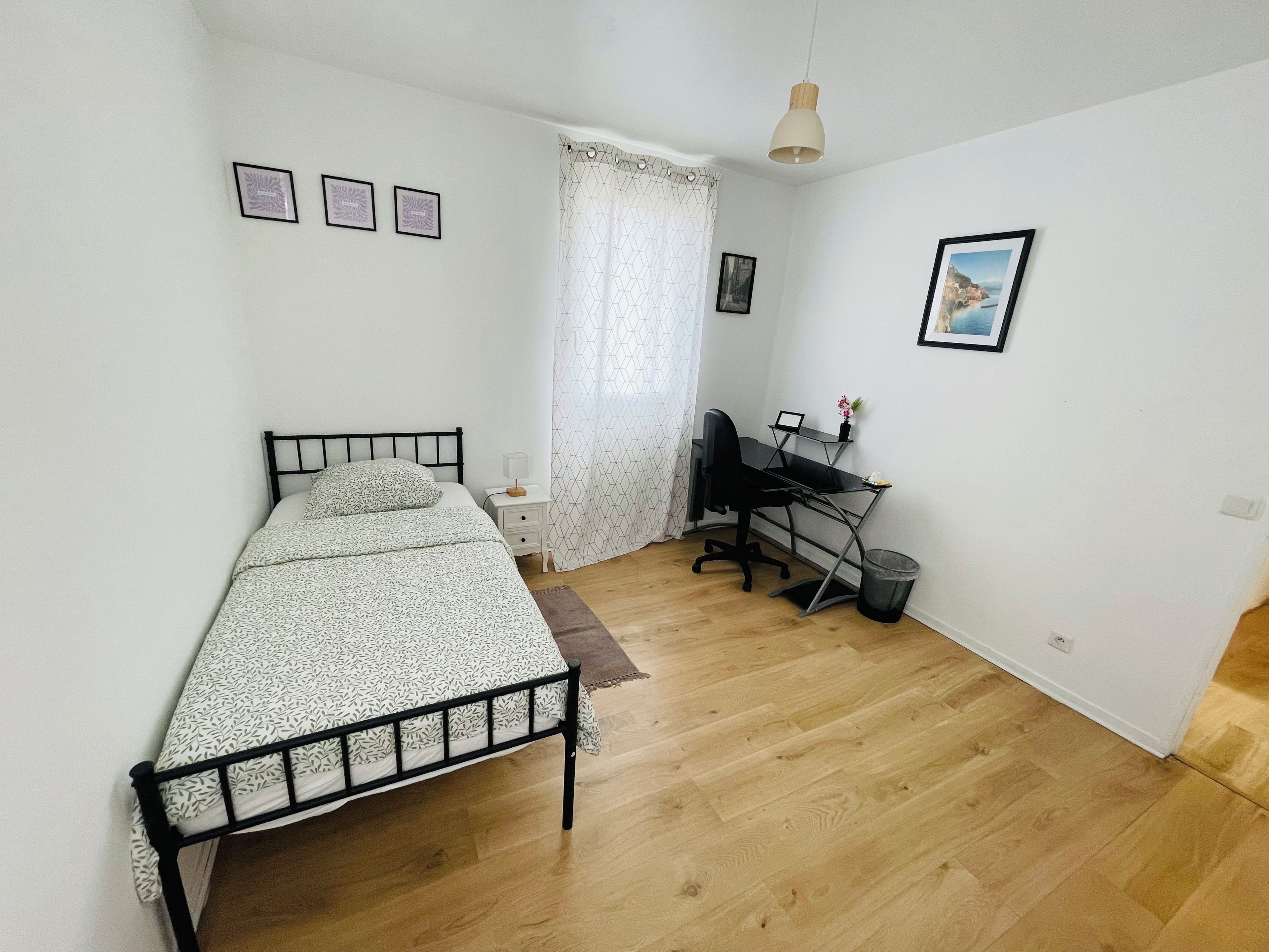 Een slaapkamer met een bed, een bureau en een stoel. Drie ingekaderde foto's hangen aan de muur.