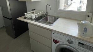 Une cuisine compacte équipée d’un lave-linge intégré, d’un réfrigérateur et d’une fenêtre donnant sur l’extérieur.