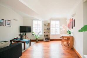 Ein Wohnzimmer mit Fernseher, einem Tisch mit Pflanze, einem Bücherregal und einem Essbereich mit Stühlen.