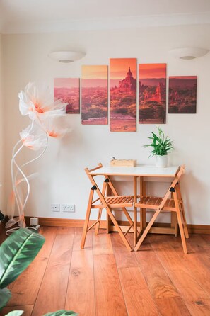 Ein Essbereich mit Holztisch und -stühlen, einem Blumentopf und einer Wand mit vier gerahmten Bildern.