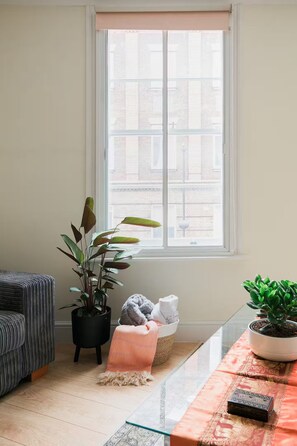 A room with a large window, a potted plant, a sofa, and a table with a rug. - Two Bedrooms Flat Near Big Ben & Westminster Abbey (London)