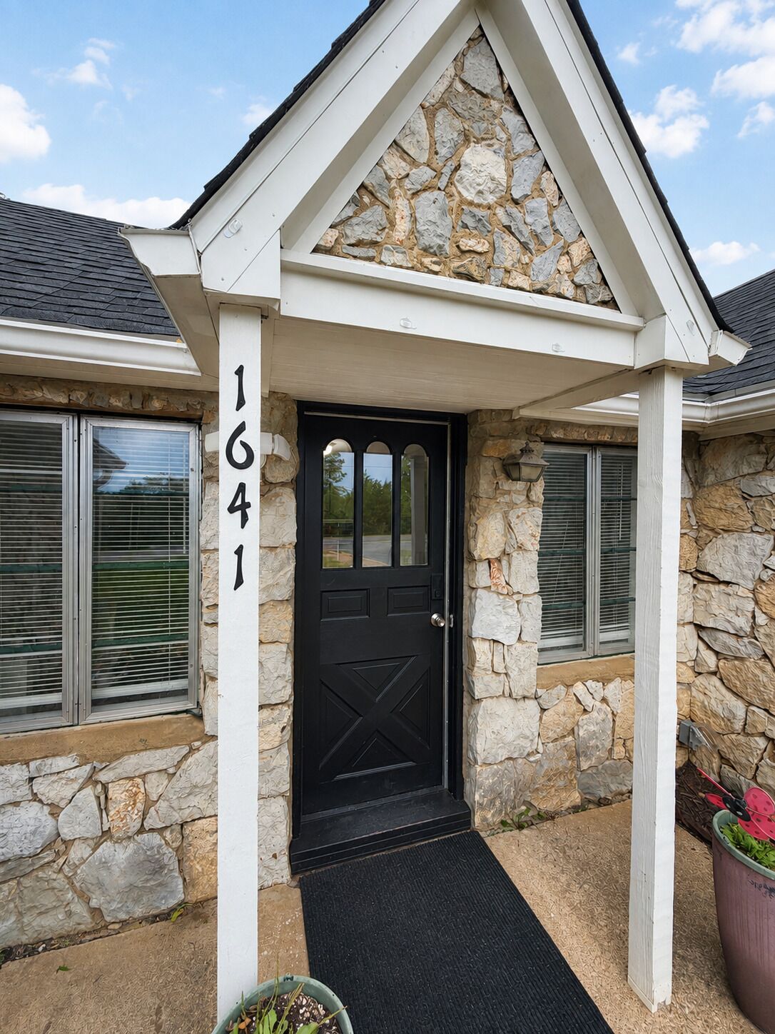 A stone house with a black door, a number '1641' on the wall, and a small porch with a black mat.