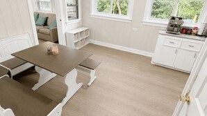 A room with a dining table, benches, a sofa, a kitchen area, and windows with a view of greenery. - The Stone House • 5 Min to JMU • Fenced Yard • Peaceful Retreat No Neighbors (Harrisonburg)