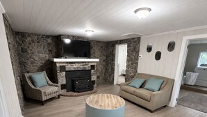 A living room with a stone wall, a fireplace, a television, and a round coffee table. - The Stone House • 5 Min to JMU • Fenced Yard • Peaceful Retreat No Neighbors (Harrisonburg)