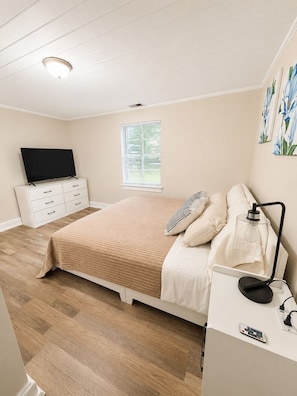 A bedroom with a bed, bedside table, lamp, TV, dresser, and window. - The Stone House • 5 Min to JMU • Fenced Yard • Peaceful Retreat No Neighbors (Harrisonburg)