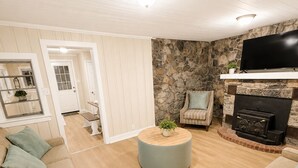 A living room with a stone wall, a fireplace, a television, and a round coffee table. - The Stone House • 5 Min to JMU • Fenced Yard • Peaceful Retreat No Neighbors (Harrisonburg)